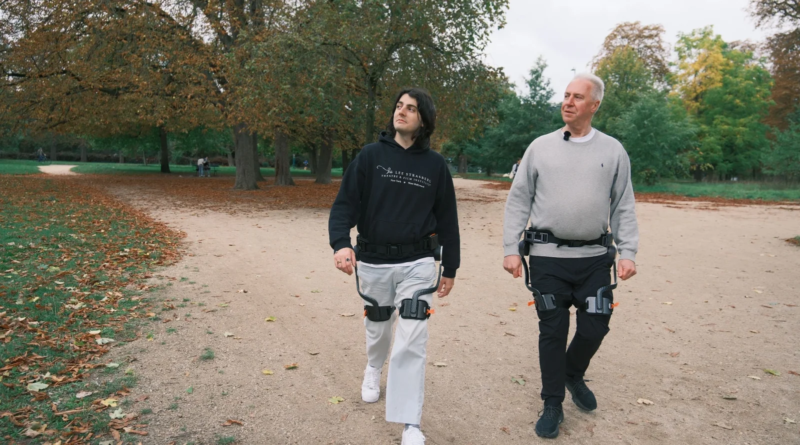 Dos personas caminando en un parque, ambas usando el exoesqueleto de cadera Ascentiz