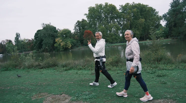 Blog lifestyle image of an active older couple walking and smiling along a scenic riverside path wearing Ascentiz hip exoskeletons, showcasing premium Mother's Day wellness gift ideas for active aging and daily walking support.