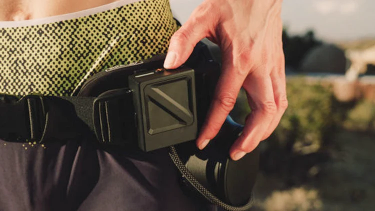 Close-up of a user's hand operating the square control module on the Ascentiz Exo-Belt Pro outdoors.