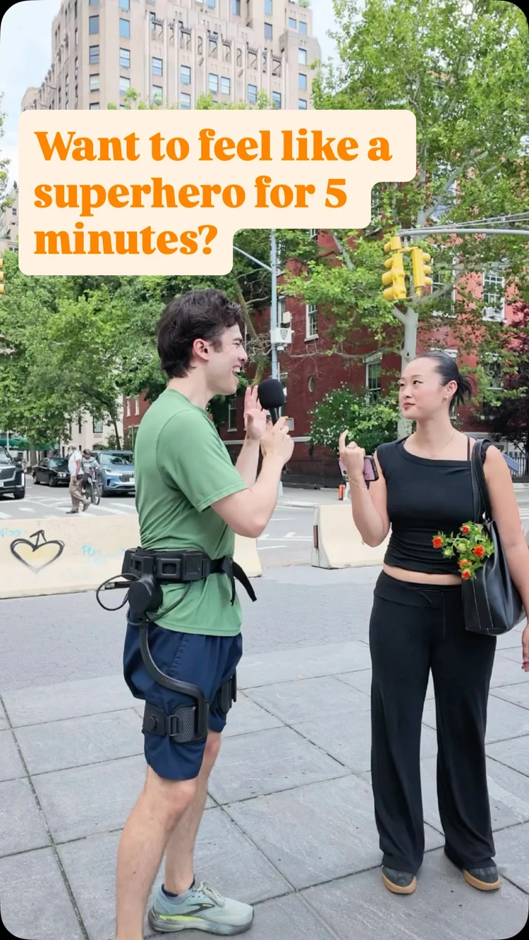A man wearing a superhero exoskeleton robot from Ascentiz stands on a city sidewalk talking to a woman.