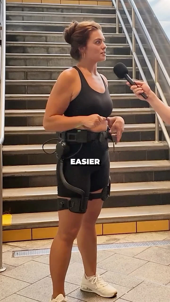 A woman wearing Ascentiz hip-assist exoskeleton device stands in front of outdoor stairs while being interviewed about her feeling.
