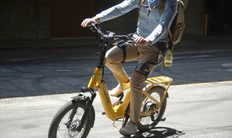 A man is riding a bike in city while wearing the Ascentiz hip exoskeleton.